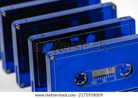 A row of blue cassette tapes with shallow depth of field. The cassette in front is in focus, while the ones stacked behind cascade out of focus
