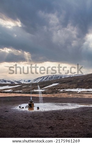Outdoor hot shower station from geothermal power at Krafla. View of black sand landscape against snow covered mountain. Scenic view of volcanic valley against cloudy sky.