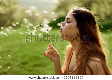 Woman with a dandelion flower in her hands smiling and blowing on it against a background of summer greenery and sunlight Royalty-Free Stock Photo #2175965907