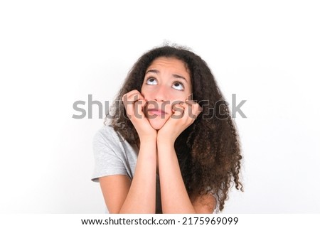 Portrait of sad young beautiful brunette teen girl wearing grey t-shirt over white wall hands face look empty space