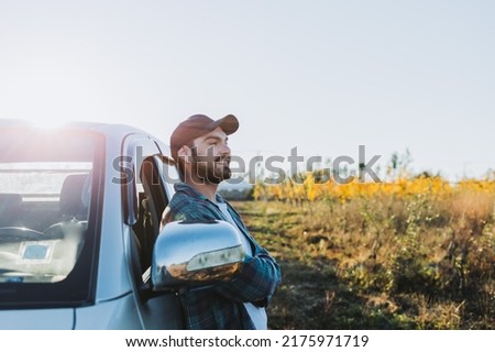 Young latin farmer man leaning on his pickup truck and looking at his plantations.  Royalty-Free Stock Photo #2175971719