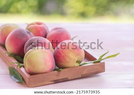 Fresh Sweet Peach on green bokeh background, Pink and yellow Peach fruit with leaf on wooden plate. Royalty-Free Stock Photo #2175973935