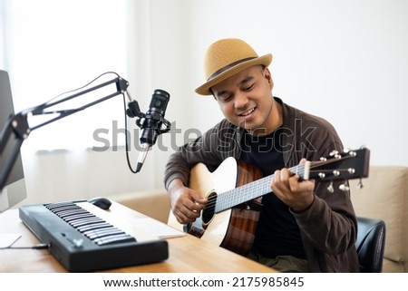 Professional Musician with condenser microphone and tablet for Mixing Mastering music. Hispanic male composing a song with guitar and piano keyboard at digital Recording home studio Royalty-Free Stock Photo #2175985845