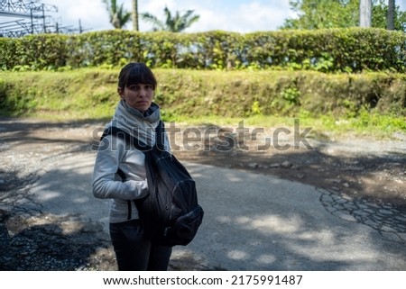 Peruvian Woman wearing a Sweatshirt and Carrying her Backpack in front her  Looks Sad in the Countryside in Filandia, Colombia 
