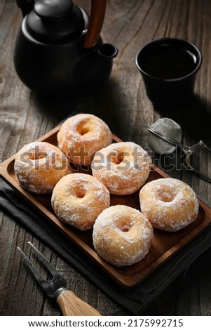 Donuts with a sprinkling of powdered sugar on the square wooden plate. served on a dark wooden background with copy space, selective focus, blurry background.