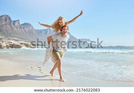 Portrait of a happy and loving young couple enjoying a day at beach in summer. Cheerful affectionate husband giving his joyful wife a piggyback while walking and having fun by the seashore on holiday Royalty-Free Stock Photo #2176022083