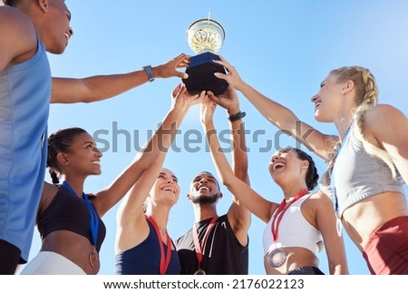 A diverse team of athletes celebrating a victory with a golden trophy and looking excited. A fit and happy team of professional athletes rejoicing after winning an award at an athletic sports event Royalty-Free Stock Photo #2176022123