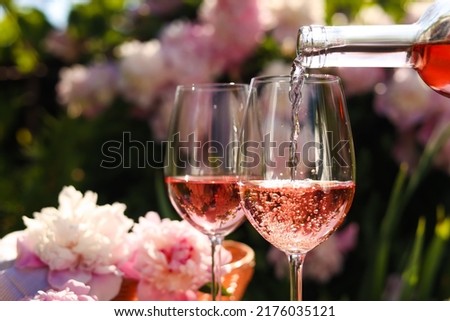 Pouring rose wine into glass in garden, closeup Royalty-Free Stock Photo #2176035121