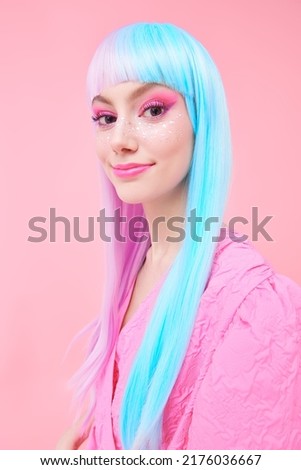 A cute girl with bright makeup and in colored violet-blue wig and pink dress poses on a pink background. Fashion. Hairstyle, hair coloring, make-up. Japanese anime style. 