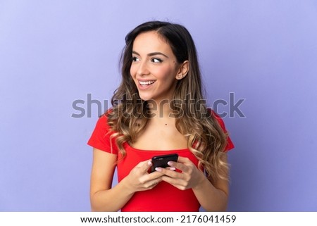 Young caucasian woman isolated on purple background using mobile phone and looking up