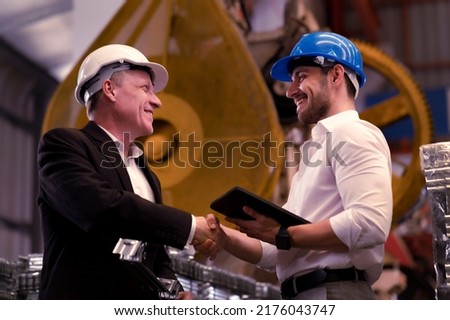 Professional engineers wear white and blue helmet for security safety in Metal Lathe heavy factory, shaking hands after deal agreement complete to produce the products and supplying the material Royalty-Free Stock Photo #2176043747