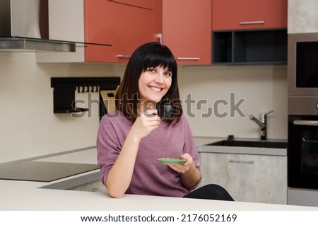 Smiling young woman with a cup in her hand in the kitchen