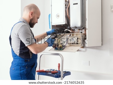 Qualified engineer checking flue gas emissions on a domestic gas boiler using a flue gas analyzer Royalty-Free Stock Photo #2176052635