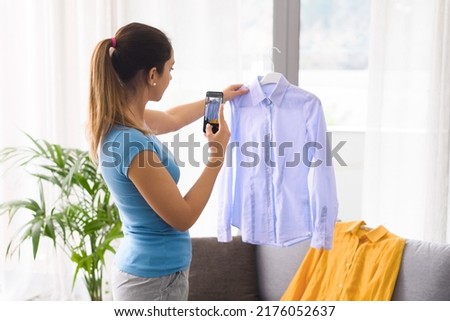 Woman taking a picture of her used shirts with her smartphone, she is selling old clothes online