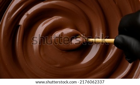 Hand stirring melted dark chocolate with golden spoon, close up. Liquid hot chocolate. Confectioner prepares chocolate dessert, glaze