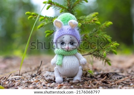 A white knitted bunny is sitting by a green Christmas tree. Knitted toys for children