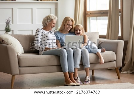 Funny movie. Happy family of 3 diverse age female members resting on sofa at home with laptop, hoary aged grandmother, her adult daughter and small grandchild girl watching comedy on computer screen Royalty-Free Stock Photo #2176074769