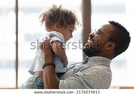 Happy daddy holding kid in arms, hugging toddler boy. African American dad enjoying being father, spending time and playing with cute preschooler son, talking to child, laughing. Parent concept Royalty-Free Stock Photo #2176074815