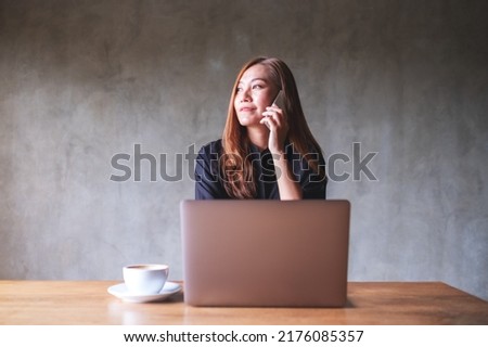 Portrait image of a businesswoman using and talking on mobile phone while working on laptop computer
