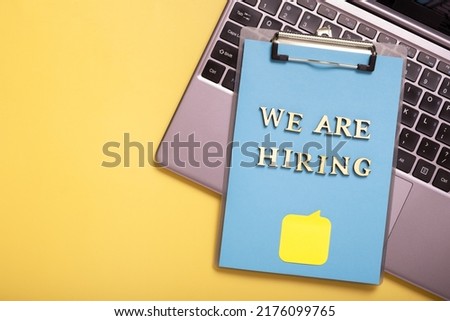 Wooden letters with phrase we are hiring on clip-board on colored background top view. Search worker concept.