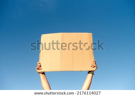 Two hands holding a cardboard sign with no content.