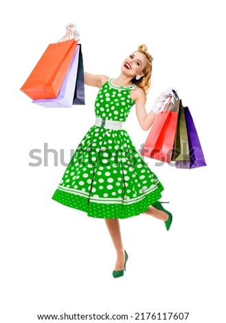 Full body of jumping, running, dancing woman in pinup style green color dress holding, showing shopping bags, isolated on white background. Sales, discounts rebates or consumer bank credit ad concept.
