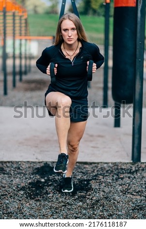 Woman in workout. Young athletic female in sportswear trains with fitness straps on sports ground.