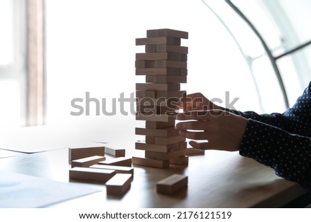 Crop close up of young female employee sit at desk in office play stack game alone. Woman worker involved in creative thinking brainstorm with wooden activity, develop logic. Creativity concept.