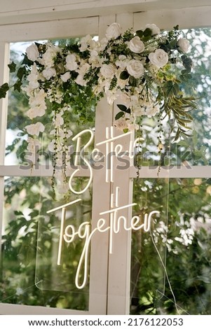 Better Together - neon sign on a window with white flowers at a wedding party. Elements of wedding decor