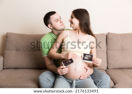 Portrait of young happy married couple hold ultrasound picture. Diverse man and pregnant woman show sonogram image on kid child, excited for parenthood. Parenting concept.