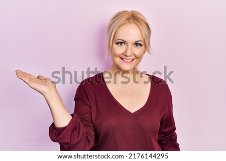 Young blonde woman wearing casual winter sweater smiling cheerful presenting and pointing with palm of hand looking at the camera. 