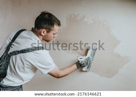 Male builder in work overalls plastering a wall using a construction trowel. Horizontal panorama banner with blank space for text. Royalty-Free Stock Photo #2176146621
