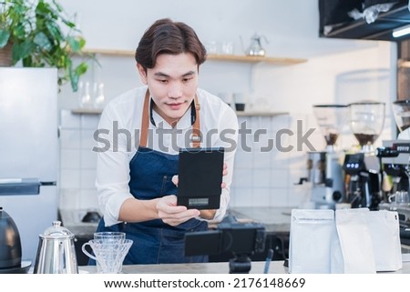 Asian businessman cafe owner record video of product for sale marketing. Handsome barista worker using camera livestreaming virtual or post advertising video for online digital social network content.