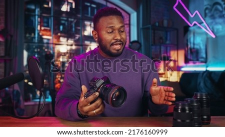 Young Handsome Black Man Recording a How To Video About New Photo Camera and Video Equipment. Entertaining Multiethnic Male Explaining New Features on Live Podcast on Social Media.