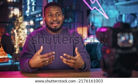 Stylish Young African American Man Talking Into Microphone While Recording Radio Show from His Loft Apartment. Happy Black Male Talking on Camera and Recording Podcast Live on Social Media.