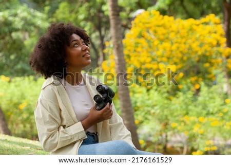 happy african american beautiful woman holding binoculars In a park with many trees. Birdwatching. Birdwatching. Look for something with binoculars. Royalty-Free Stock Photo #2176161529