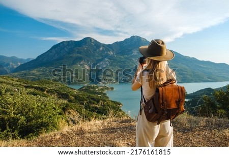 Woman photographer with big backpack taking photo of mountains and blue lake. Travel and hobby concept Royalty-Free Stock Photo #2176161815
