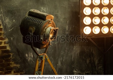 Vintage retro lighting equipment for shooting and movie. Old rust-worn steel large lamp stands on a rack near a light panel. Grunge brick walls in loft style. High quality shot