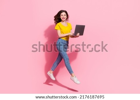 Full length photo of impressed millennial brunette lady run with laptop wear t-shirt jeans sneakers isolated on pink background