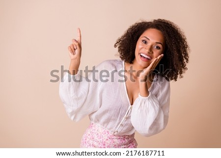 Photo of pretty excited lady wear white top arm cheek pointing up empty space isolated beige color background
