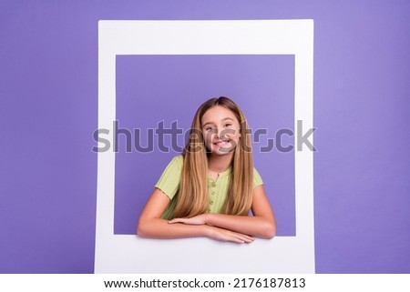 Portrait of adorable friendly pupil toothy smile look through paper album card isolated on purple color background