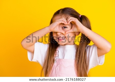 Photo of pretty funny school girl wear summer overall arms showing heart cover eye isolated yellow color background