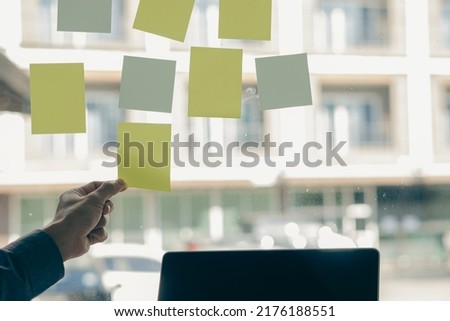 Businessman posting notes on glass wall. Businessman hands recording work on a memory stick on the glass. creative ideas are written on sticky paper at the office Royalty-Free Stock Photo #2176188551