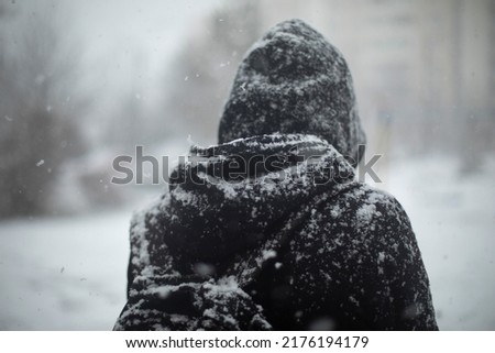 Man outside in snowfall. Black clothes in snow. Guy is standing in middle of town. Blizzard in city.