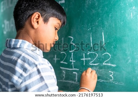 intelligent elementary school kid solving maths problem on chalkboard at classroom -concept of talented, brilliant student and education. Royalty-Free Stock Photo #2176197513