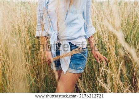 Young woman walking in meadow picking grasses wearing linen shirt and jeans shirts. Natural summer clothes.