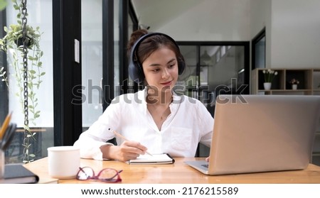 asian woman interpreter write translation from foreign language to english listen to audio record in headset. 

