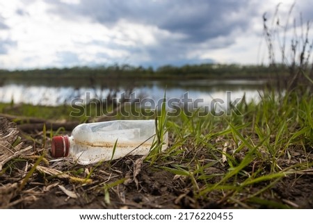 Abandoned garbage waste on nature. Environmental damage caused by human garbage pollution. Left plastic bottle among the grass on the river bank Royalty-Free Stock Photo #2176220455