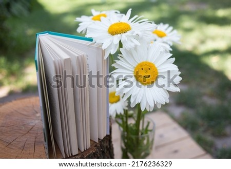 book, open pages and a bouquet of daisies in a vase, one of the flowers - with a smile. Calm morning picture. Rest and reading. Read a book with pleasure. Cozy atmosphere in the garden