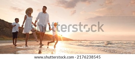Happy family running on sandy beach near sea at sunset, space for text. Banner design Royalty-Free Stock Photo #2176238545